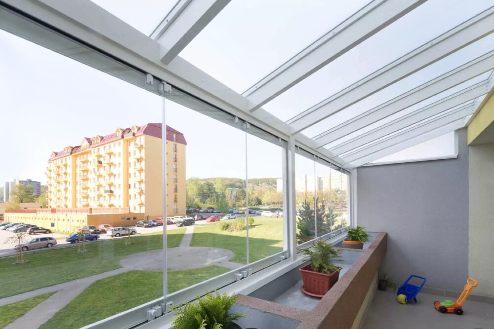 Moderne rahmenlose Balkonverglasung mit Blick auf die Wohnsiedlung und die Grünflächen