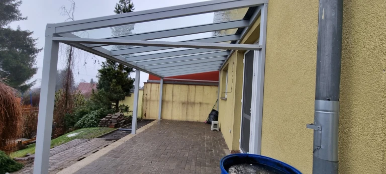 Moderne graue Aluminium-Pergola LIGHT mit Glasdach, an der Hauswand über der Terrasse angebracht