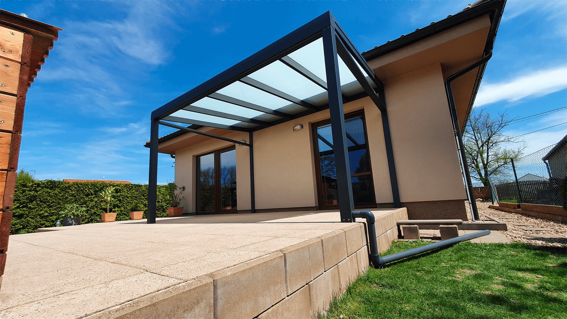 Moderne anthrazitfarbene Aluminium-Pergola mit verglastem Dach auf der Terrasse eines Einfamilienhauses