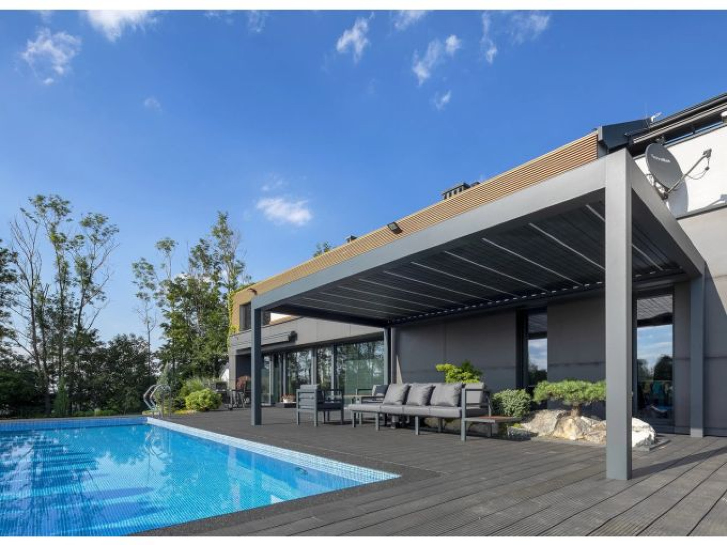 Die moderne, graue, bioklimatische Pergola SUNBEAM 1400 auf der Terrasse am Pool mit Sitzgelegenheiten im Außenbereich