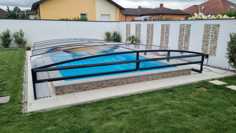 Moderne, niedrige Schwimmbadüberdachung mit schwarzer Konstruktion und transparenter Verkleidung im Garten