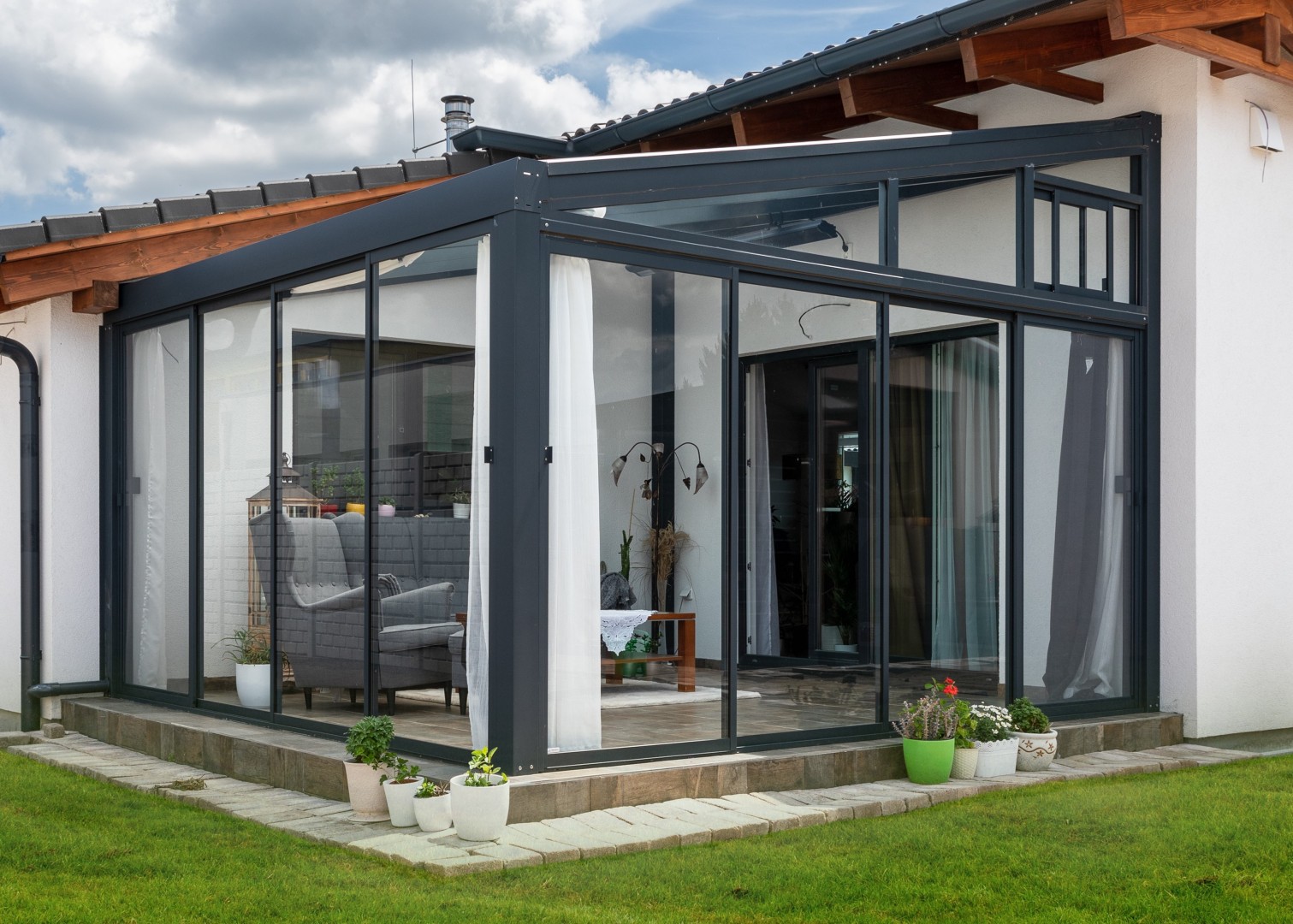 Eine moderne, verglaste Aluminium-Pergola, die an das Haus angebaut ist und über eine elegante Innenausstattung verfügt.
