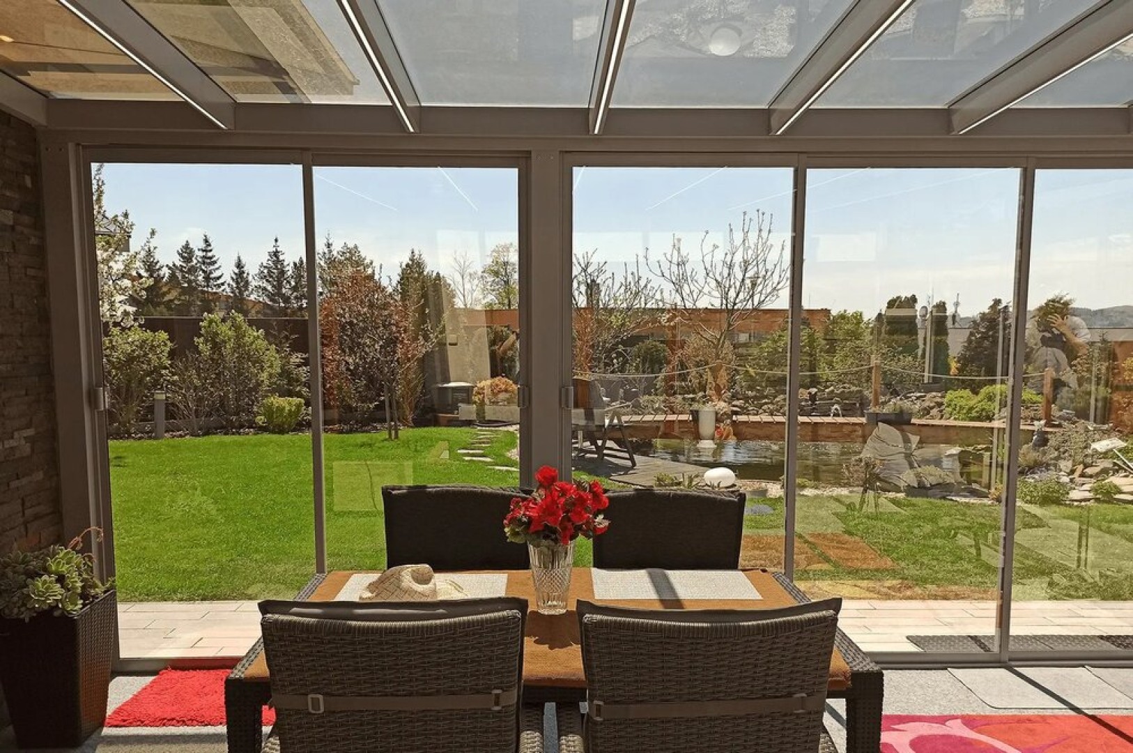 Verglaste Terrasse mit Blick auf den Garten, mit Sitzgelegenheiten und Blumen