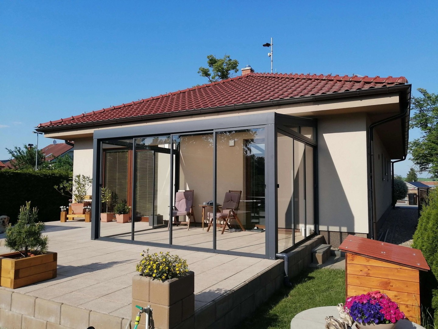 Ein moderner, verglaster Wintergarten mit anthrazitfarbener Konstruktion auf der Terrasse eines Einfamilienhauses