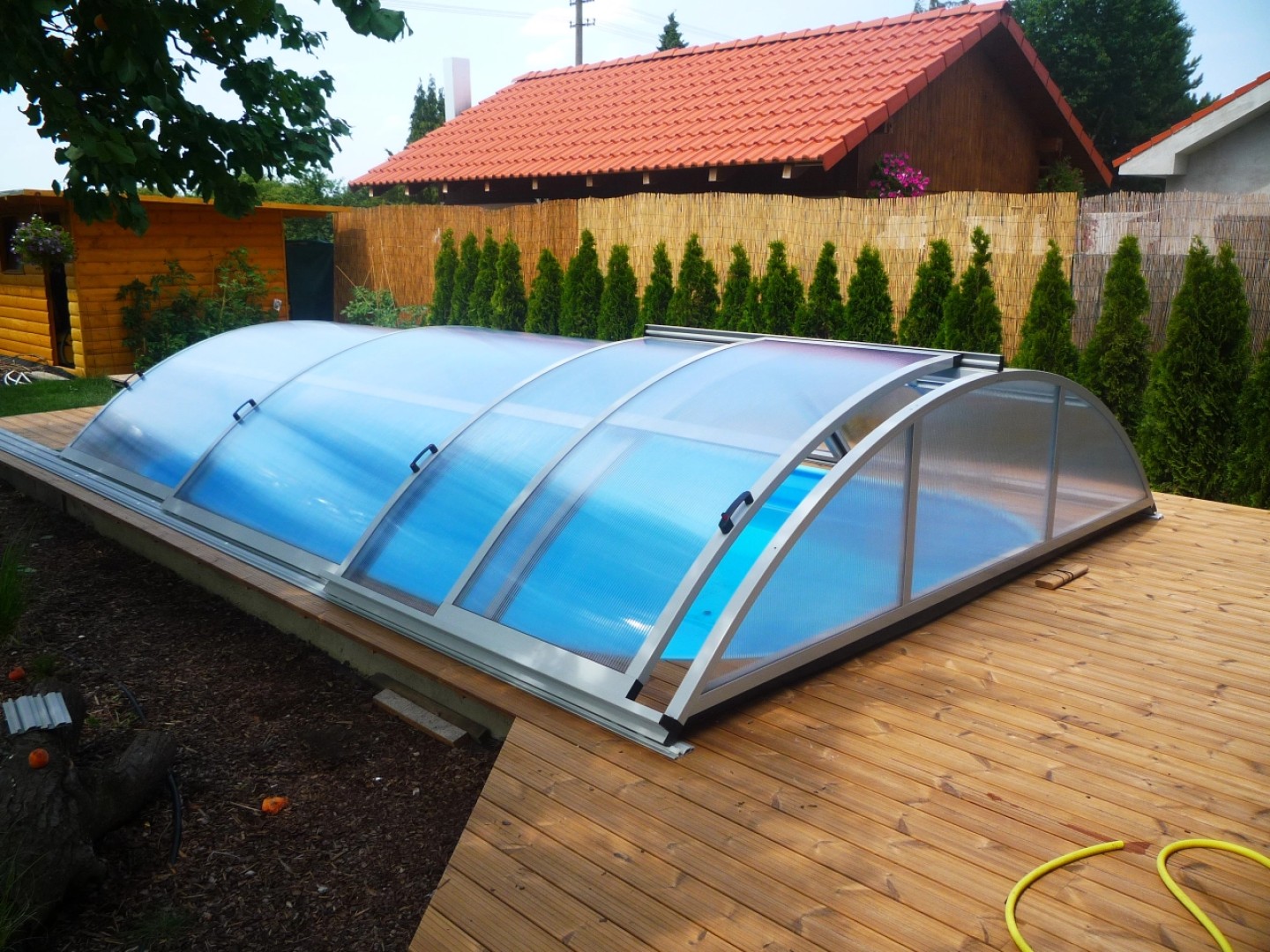 Niedrige, gewölbte Überdachung des Schwimmbeckens auf einer Holzterrasse im Garten