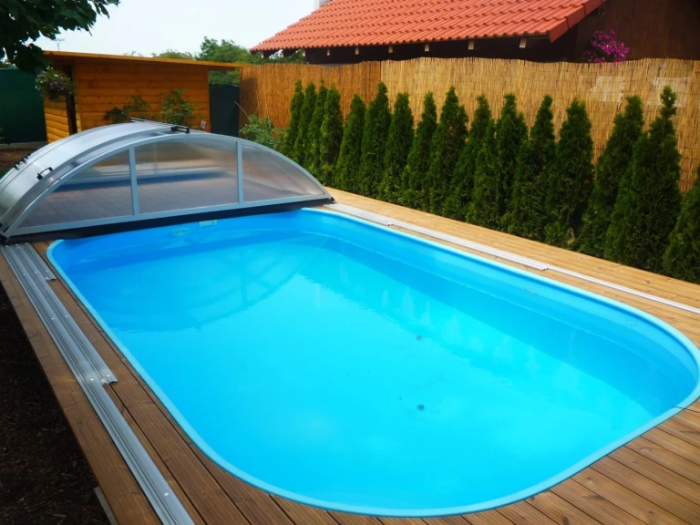 Ein blauer Pool mit Holzverkleidung und einer teilweise zu öffnenden Schiebeabdeckung im Garten.