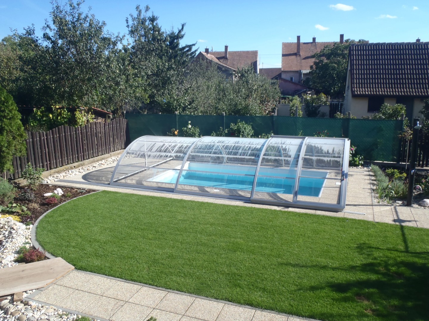 Eine moderne, niedrige Überdachung für das Schwimmbecken im Garten eines Einfamilienhauses mit Rasenfläche.