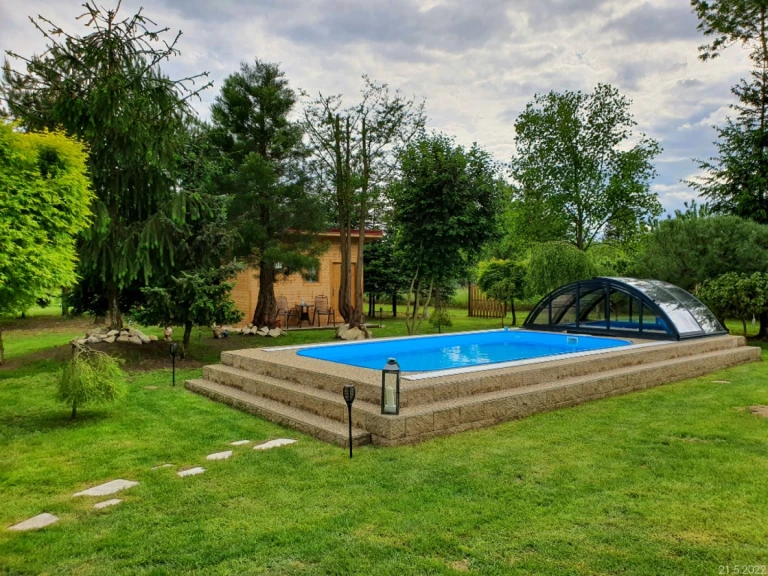 Ein Gartenpool mit blauer Folie und einer niedrigen Schiebeabdeckung auf einer erhöhten, von Grün umgebenen Terrasse.