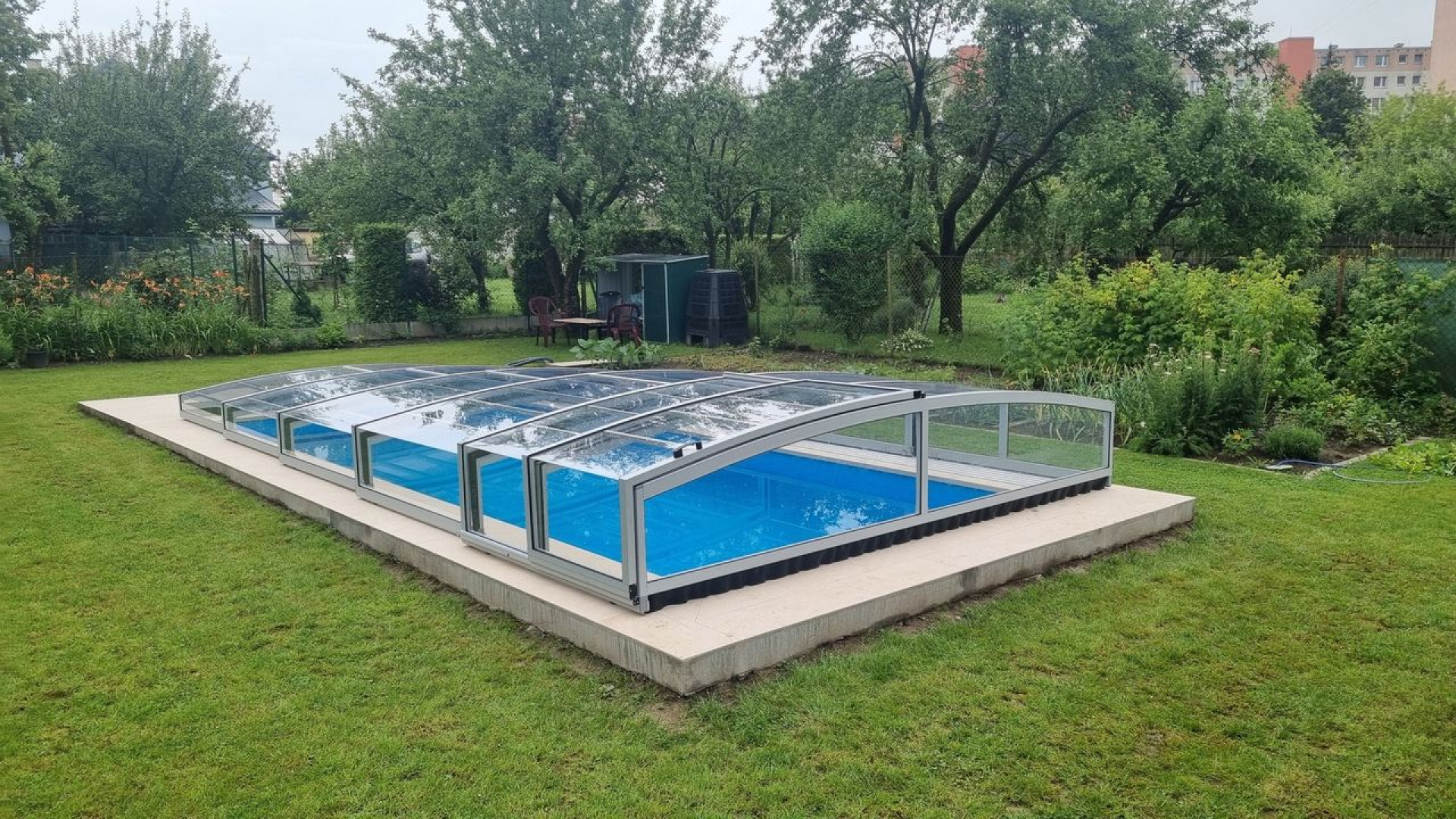 Die niedrige PREMIER-Schwimmbadüberdachung über dem blauen Pool im Garten in Martin.