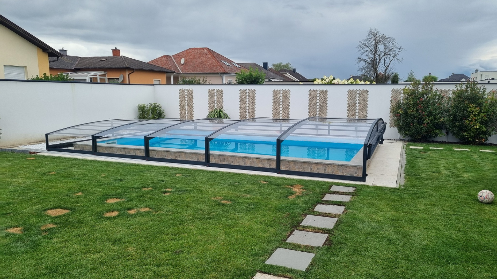 Moderne, niedrige Schwimmbadüberdachung in Anthrazit im Garten mit Rasenfläche