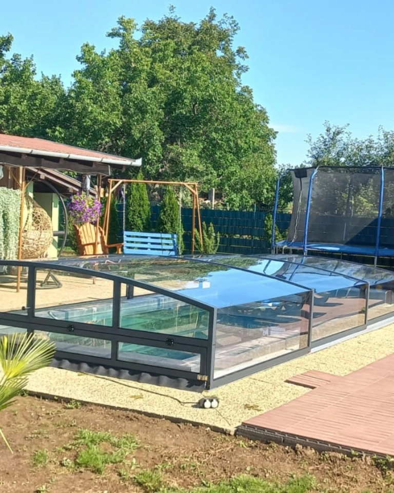 Moderne, niedrige Schwimmbadüberdachung mit anthrazitfarbenem Rahmen im Garten