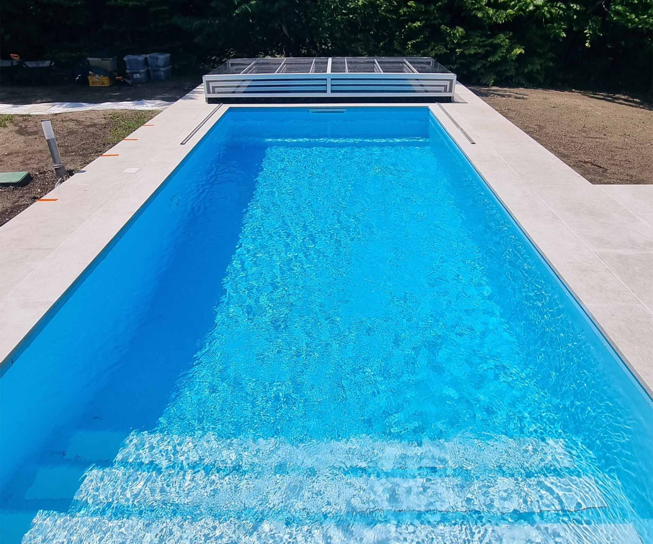 Ein moderner, rechteckiger Pool mit strahlend blauem Wasser und einer eleganten weißen Einfassung im Garten.