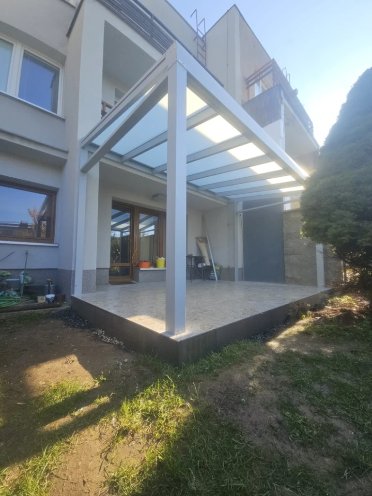 Eine moderne weiße Aluminium-Pergola mit milchiger Verglasung, errichtet auf der Terrasse eines Einfamilienhauses