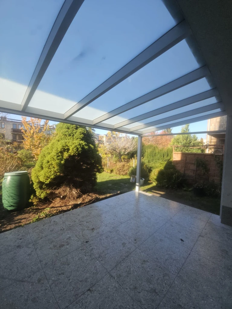 Eine moderne Aluminium-Pergola mit Glasdach über der Terrasse mit Blick auf den Garten.