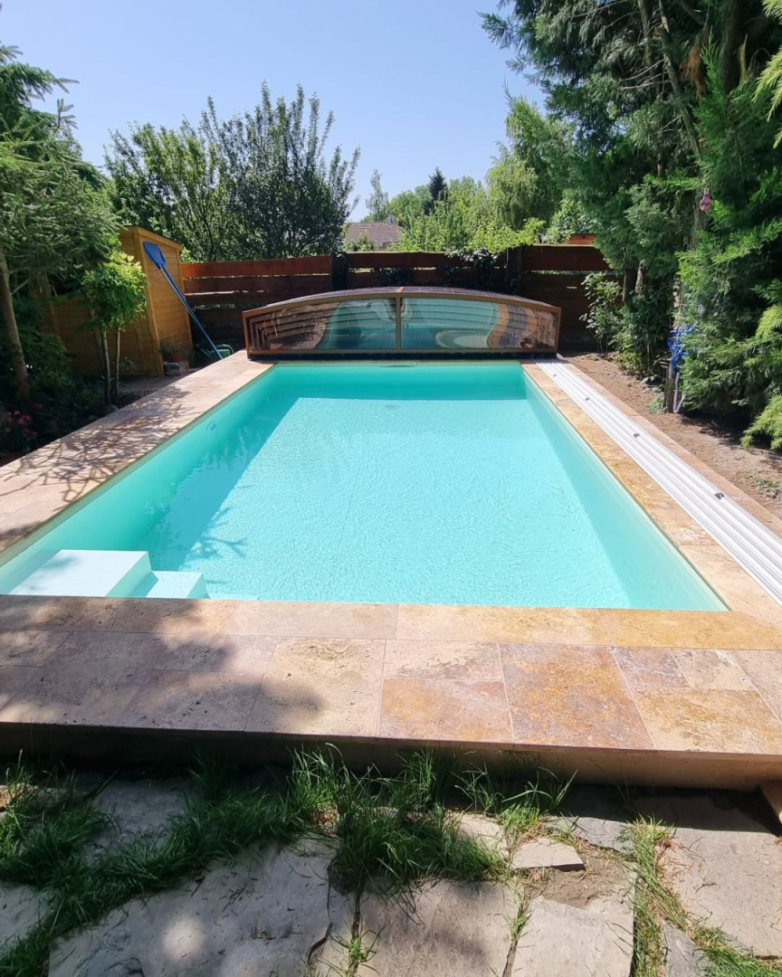 Ein modernes Schwimmbecken mit klarem, türkisfarbenem Wasser und einer niedrigen Schiebeüberdachung im Garten.