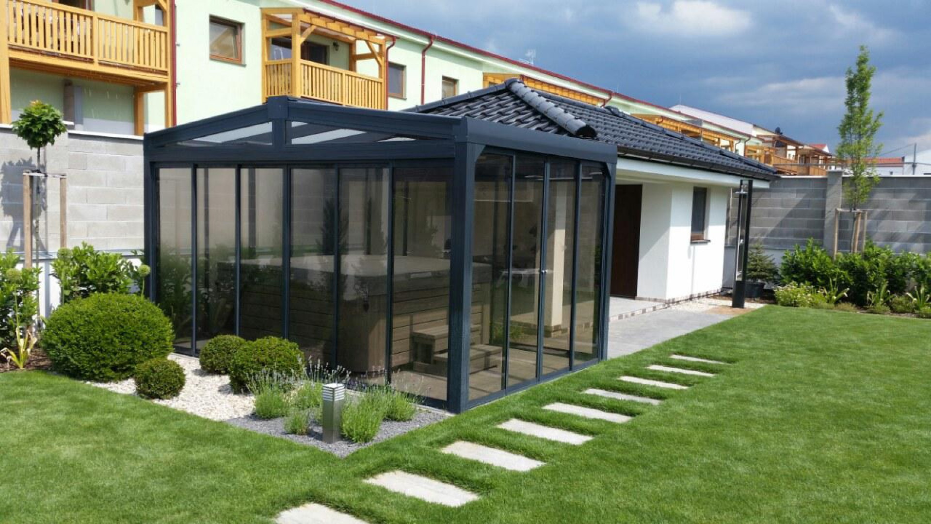Ein moderner, verglaster Whirlpool-Unterstand mit dunkler Konstruktion im gepflegten Garten neben dem Haus.