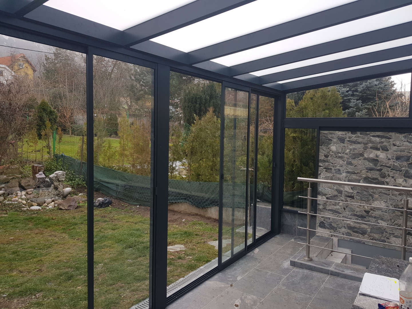 Ein moderner, verglaster Wintergarten mit Aluminiumkonstruktion und Schiebetüren mit Blick in den Garten