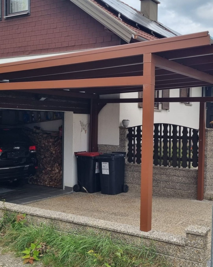 Ein brauner Carport neben einem Einfamilienhaus mit Garage und Mülltonnen