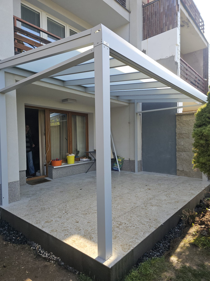 Eine moderne Aluminium-Pergola mit Glasdach auf der Terrasse eines Einfamilienhauses
