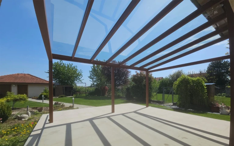 Blick von unterhalb der verglasten Aluminium-Pergola auf den Garten mit dem Einfamilienhaus