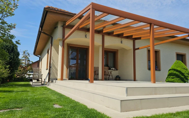 Eine braune Aluminium-Pergola mit Glasdach, die auf der Terrasse eines Einfamilienhauses montiert ist