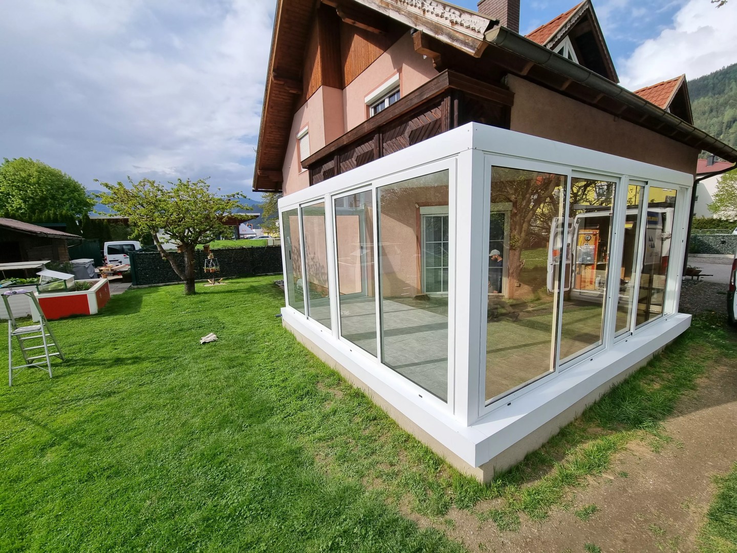 Eine moderne, weiße, verglaste Aluminium-Pergola im Garten eines Einfamilienhauses.