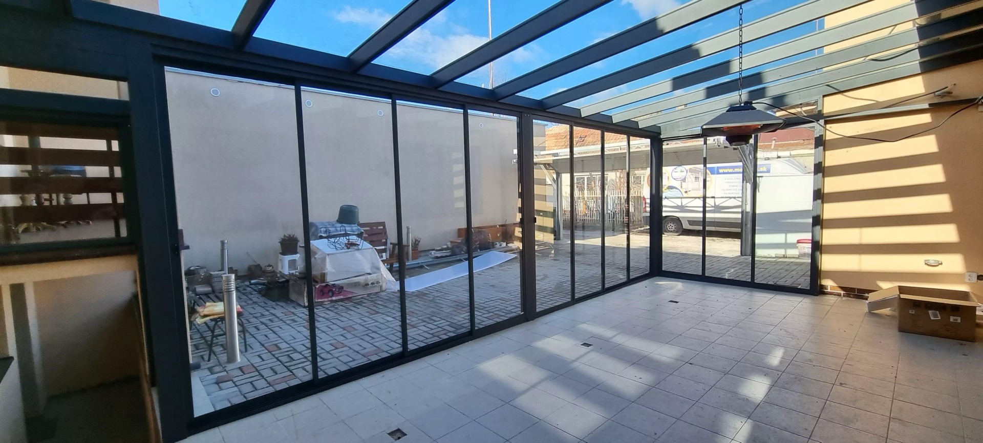 Blick von innen auf die verglaste Aluminium-Pergola ROBUST mit Schiebeverglasung auf der Terrasse eines Einfamilienhauses.