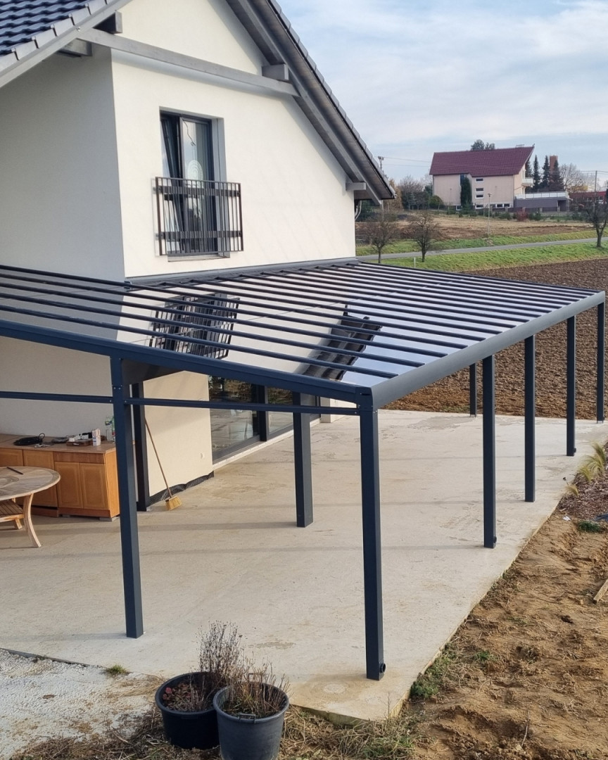Eine moderne, dunkelgraue Aluminium-Pergola mit Glasdach, die an einem Einfamilienhaus in Senec angebracht wurde.