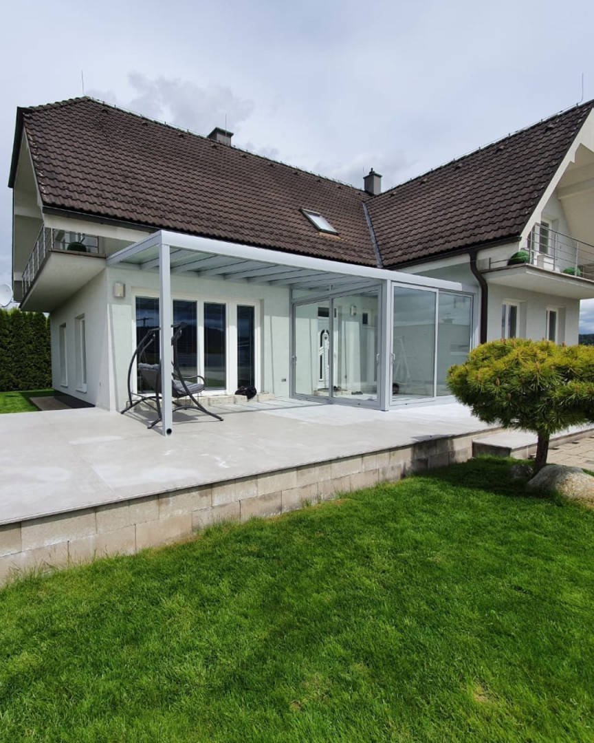 Ein moderner Wintergarten aus Aluminium mit verglasten Schiebewänden, der an ein Einfamilienhaus mit Terrasse angebaut wurde.