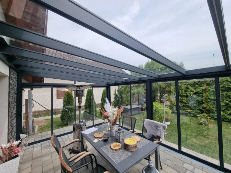 Ein moderner, verglaster Wintergarten mit anthrazitfarbener Aluminiumkonstruktion, einem Esstisch und Blick ins Grüne