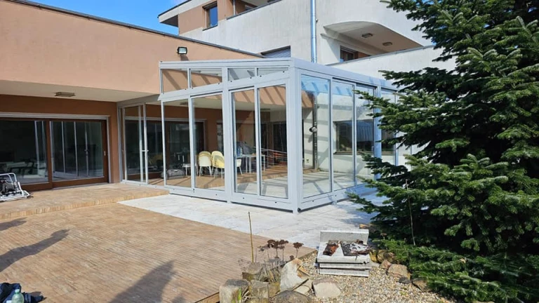 Ein moderner Wintergarten aus Aluminium mit Glasschiebetüren, der an ein Einfamilienhaus angebaut wurde