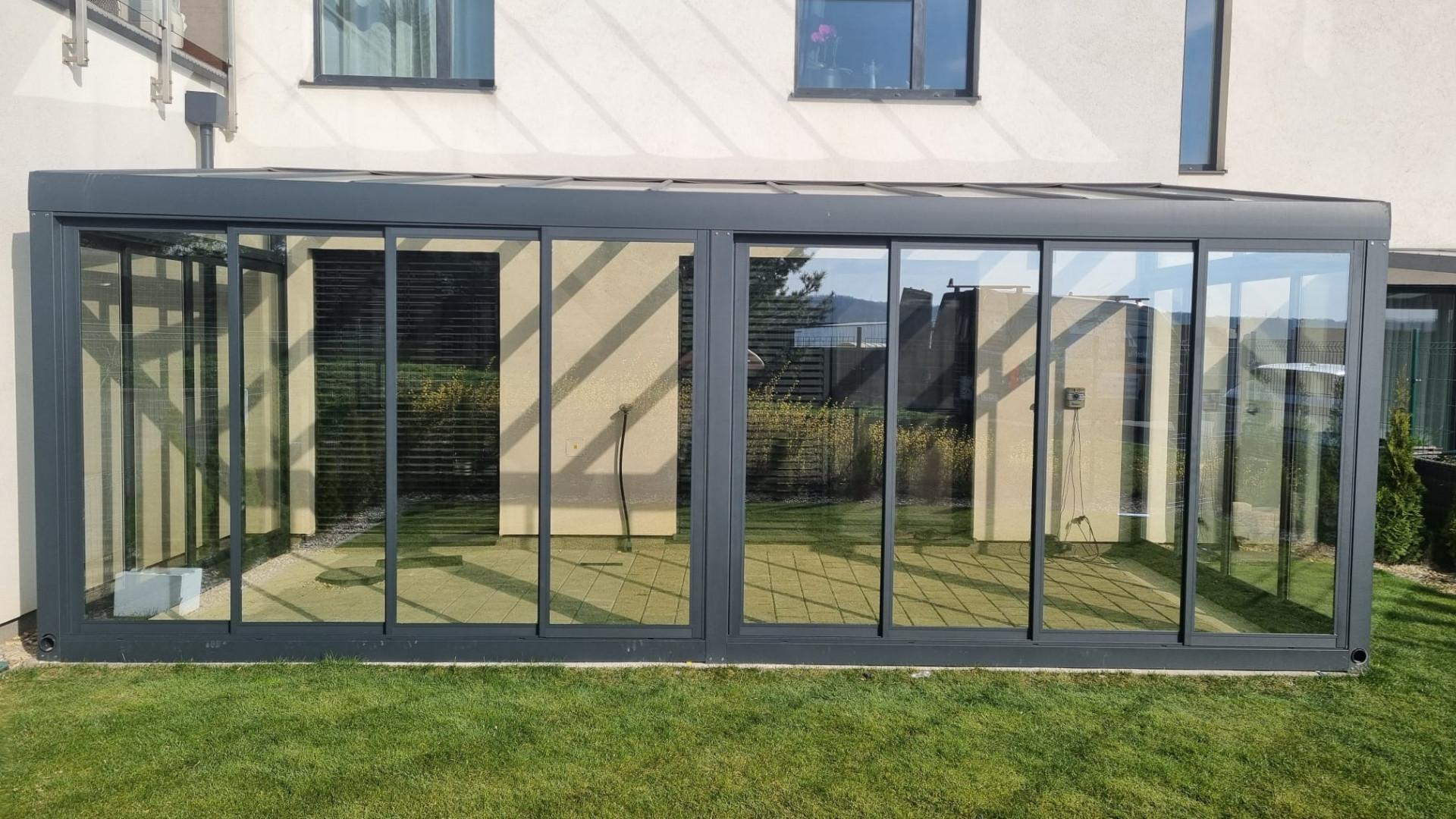 Ein moderner, verglaster Wintergarten aus Aluminium an einem Einfamilienhaus mit Blick auf den Rasen.
