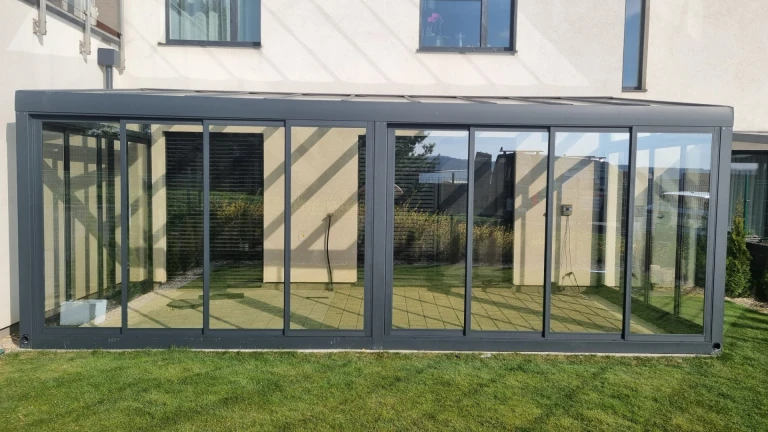 Ein moderner, verglaster Wintergarten aus Aluminium an einem Einfamilienhaus mit Blick auf den Rasen.