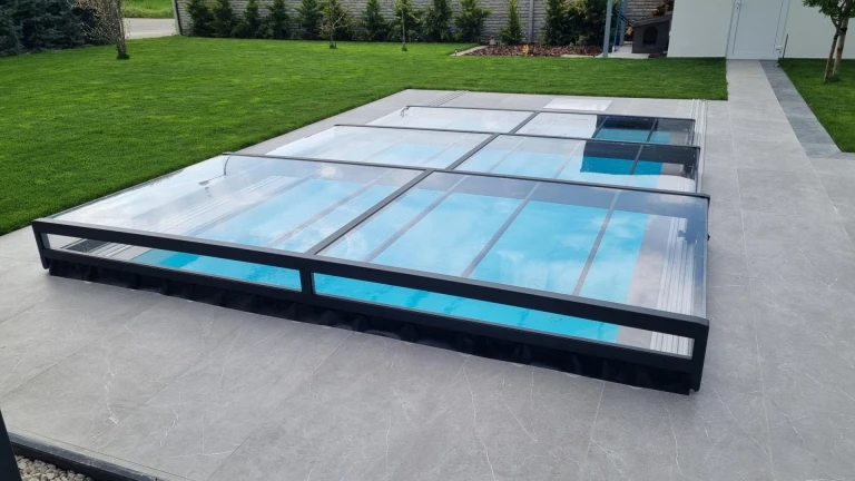Moderne, niedrige Schwimmbadüberdachung aus Aluminium mit anthrazitfarbenem Rahmen und klarem Glas im Garten
