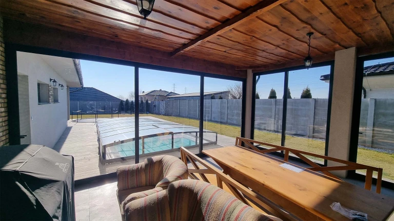 Blick von der verglasten Terrasse mit Holzdecke auf den Garten mit Swimmingpool