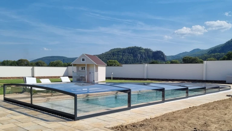 Eine moderne, niedrige, verglaste Schwimmbadüberdachung im Garten mit Blick auf die Berge und einem Gartenhäuschen.