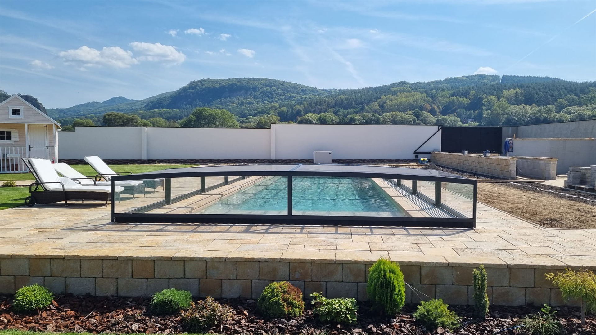 Eine moderne, niedrige Aluminium-Schwimmbadüberdachung im Garten mit Blick auf die Hügel