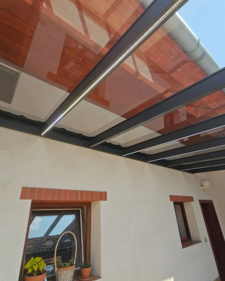 Detailansicht der Überdachung einer Aluminium-Pergola mit integrierter LED-Beleuchtung, die an der Hausfassade befestigt ist.