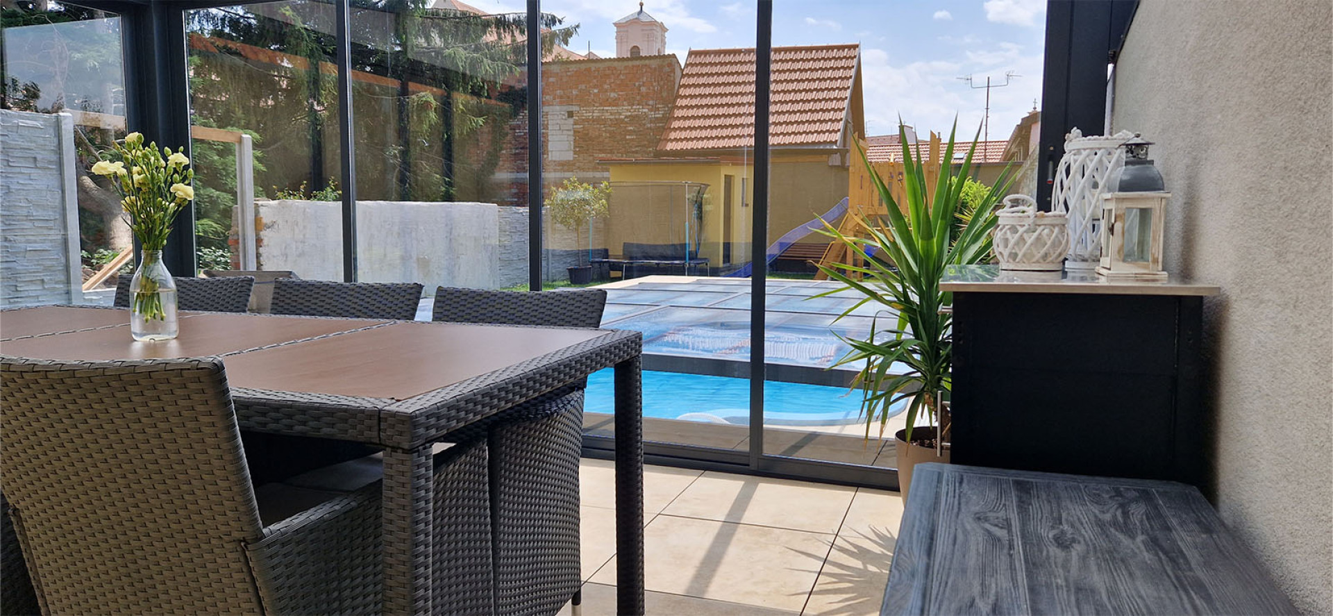 Blick aus dem Wintergarten mit Gartenmöbeln auf die Terrasse mit Pool