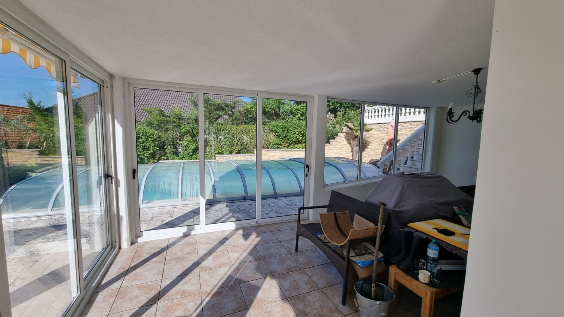 Verglaste Terrasse mit weißen Rahmen und Blick auf den Pool im Garten