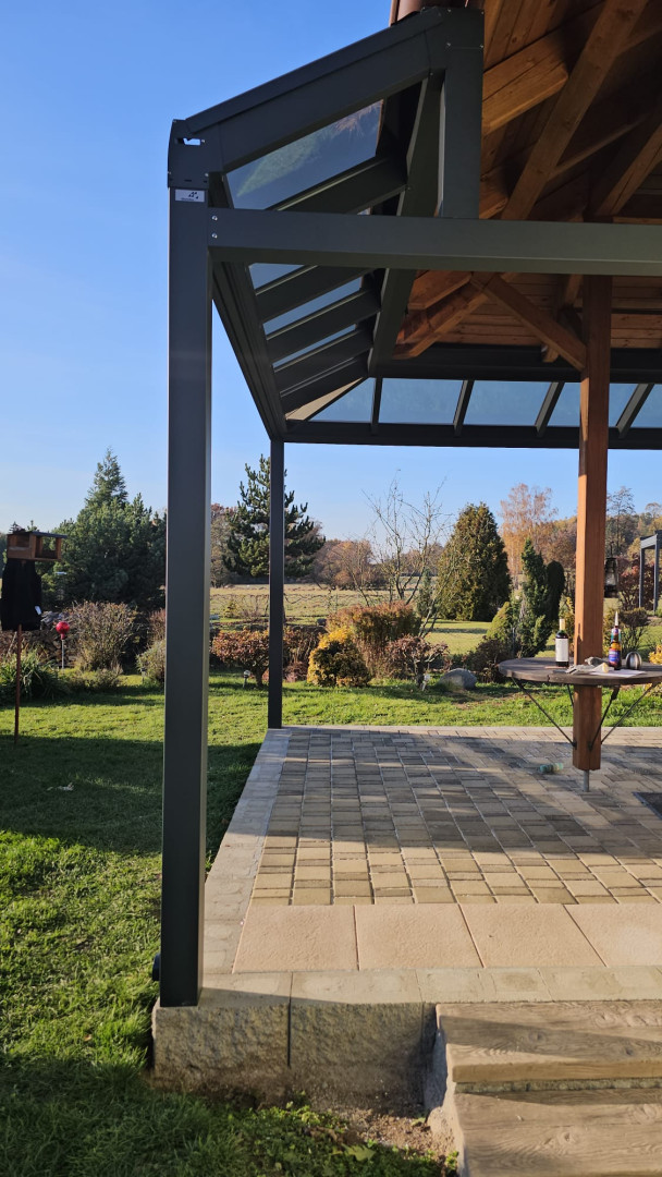 Ein detaillierter Blick auf die Aluminiumkonstruktion und das verglaste Dach der Pergola mit Blick auf den Garten.
