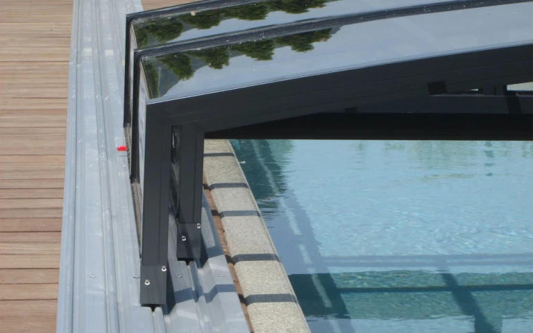 Ein detaillierter Blick auf die Aluminiumkonstruktion und die Schienen der Schwimmbadüberdachung auf der Holzterrasse.