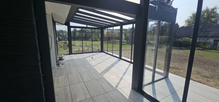 Ein moderner, verglaster Wintergarten mit anthrazitfarbener Konstruktion und hellem Bodenbelag.