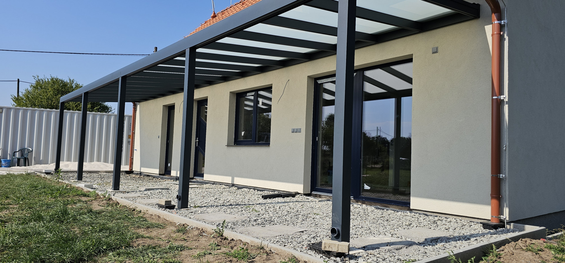 Eine moderne Aluminium-Pergola mit Glasdach, die an der Wand eines Einfamilienhauses befestigt ist