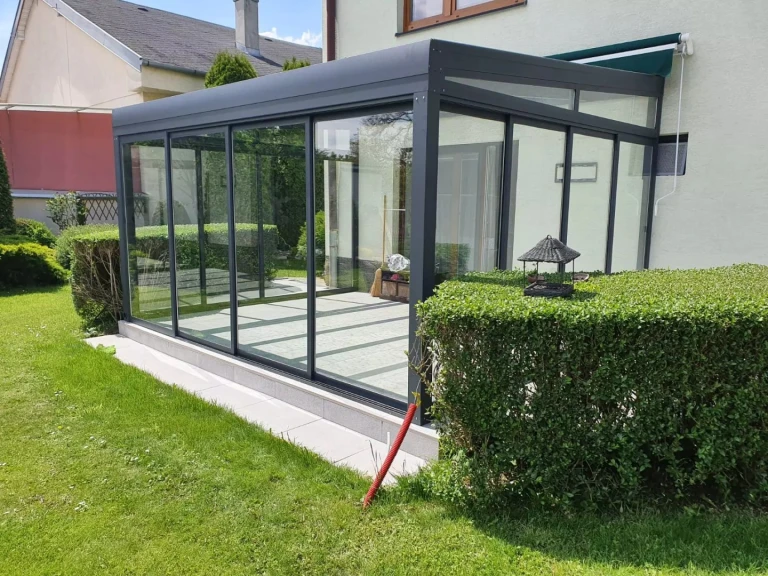 Ein moderner, verglaster Wintergarten mit anthrazitfarbener Aluminiumkonstruktion, der im Garten eines Einfamilienhauses errichtet wurde