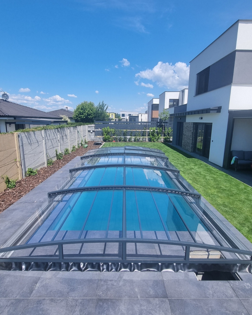 Moderne, niedrige Poolüberdachung in Anthrazit im Garten eines Einfamilienhauses mit Rasenfläche
