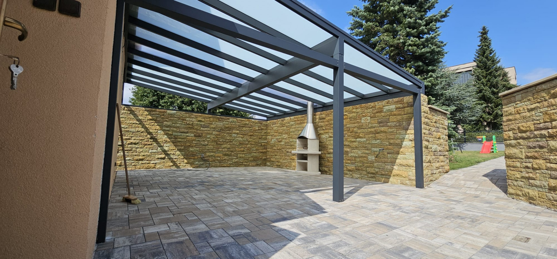 Eine moderne Terrassenüberdachung aus Aluminium mit verglastem Mittelteil, Steinverkleidung an den Wänden und einem Außenkamin.