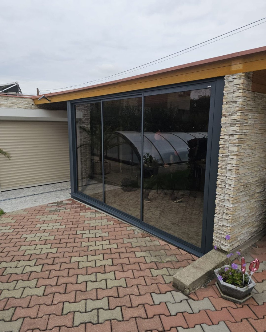 Moderne verglaste Schiebetüren auf der Terrasse mit anthrazitfarbenem Rahmen und Steinverkleidung.