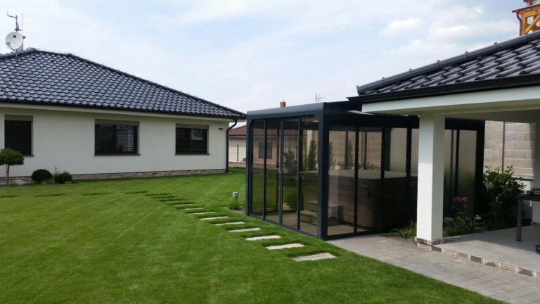 Ein moderner, verglaster Unterstand mit Whirlpool im gepflegten Garten eines Einfamilienhauses.