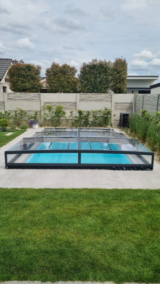 Eine niedrige, moderne Schwimmbadüberdachung in Anthrazit im Garten eines Einfamilienhauses.
